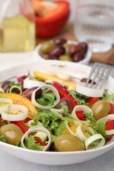 Bowl of tasty salad with leek and olives on light table, closeup