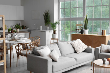 Interior of light open space kitchen with cozy grey sofa and oranges on wooden coffee table