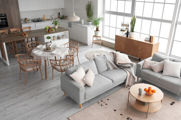 Interior of light open space kitchen with cozy grey sofas and oranges on wooden coffee table