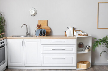 White kitchen counters with cutting boards, plate rack, sink and utensils