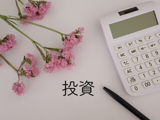 投資の文字と電卓、ピンクの花