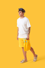 Fototapeta premium Young man with snorkeling mask and flippers on yellow background