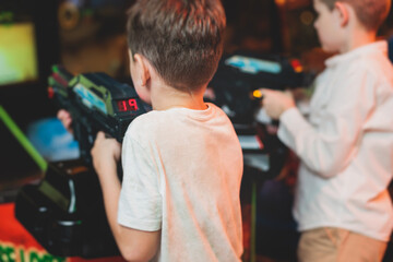 Kids play slot machine at amusement theme park, children play arcade gaming machine, racing and shooting game at the fair, teenagers having fun playing simulator video games