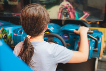 Kids play slot machine at amusement theme park, children play arcade gaming machine, racing and shooting game at the fair, teenagers having fun playing simulator video games