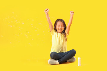 Happy little girl and soap bubbles on yellow background