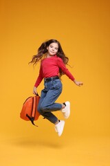 Back to school. Cute girl with backpack jumping on orange background