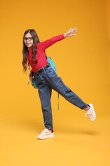 Cute schoolgirl in glasses on orange background