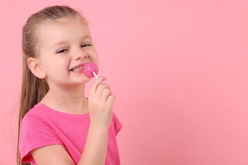 Happy little girl licking lollipop on pink background, space for text