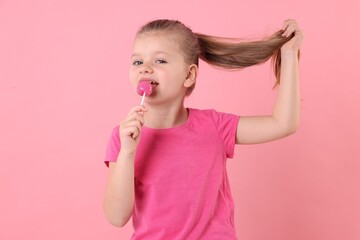 Cute little girl licking lollipop on pink background