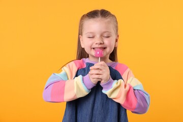 Happy little girl with lollipop on orange background