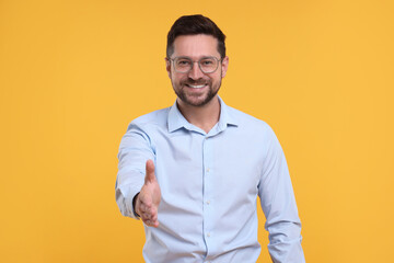 Happy man welcoming and offering handshake on yellow background - obrazy, fototapety, plakaty