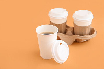 Takeaway paper cups of tasty coffee and holder on beige background