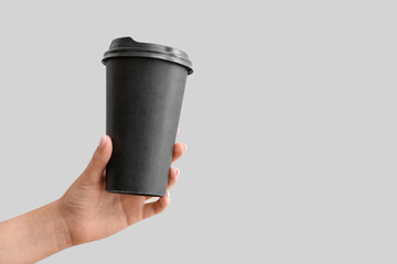 Female hand with black takeaway paper cup on light background