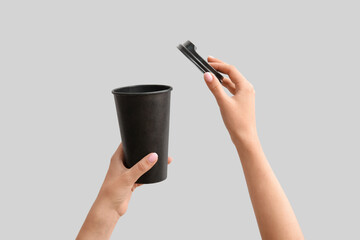 Female hands with black takeaway paper cup and lid on light background