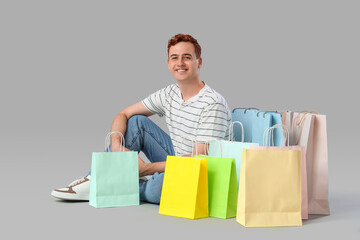 Young man with shopping bags sitting on light background