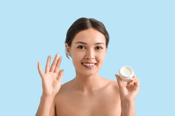 Obraz na płótnie Canvas Beautiful Asian woman with jar of cream on blue background, closeup