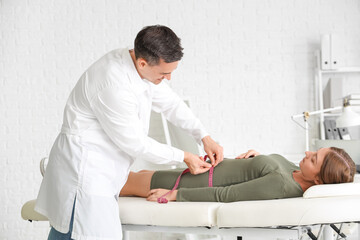 Male doctor measuring belly of pregnant woman in clinic