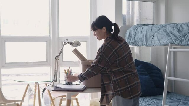 Happy young Asian Female A college student is moving in a dormitory unpacking her staff or packing for moving out of the dorm in a student dorm or to a new rented apartment.