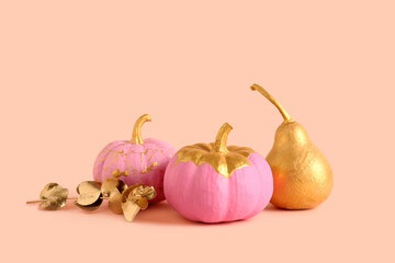Pink painted pumpkins with golden pear and leaves on orange background