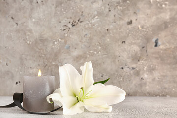 Obraz na płótnie Canvas Beautiful lily, black ribbon and burning candle on grey grunge background