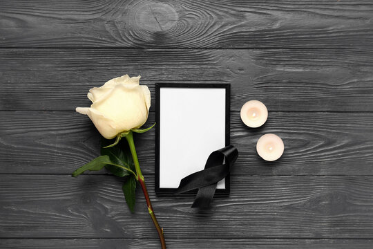 Beautiful white rose with photo frame and candles on black wooden background