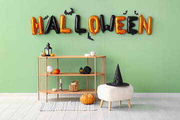 Word HALLOWEEN made of balloons with paper bats on green wall in living room interior