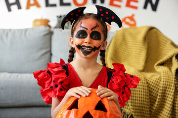 Little girl dressed for Halloween as devil with pumpkin at home