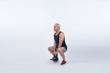 Full body length shot athletic and sporty senior man doing squat with kettlebell for body workout on isolated background. Healthy active physique and body care lifestyle after retirement. Clout