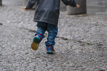 Boy running in rain on downtown cobblestone street.