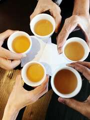Hands holding a cup of tea and cheers or celebrations together, top views, close up, reunions