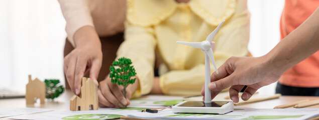 Obraz na płótnie Canvas Windmill model represented using renewable energy placed during presenting green business on table with wooden block and environmental document scatter around. Closeup. Delineation.