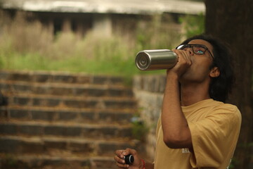 An Indian boy drinking water from a steel bottle with a blurred background in bright sunlight