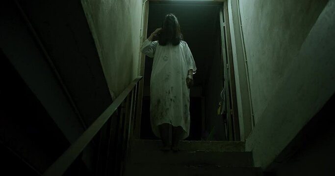Horror scene of a mysterious Scary Asian ghost woman creepy have hair covering the face standing on staircase at abandoned house with background dark scene movie at night, festival Halloween concept