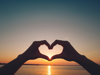 A heart shpa made with 2 hands, with an open natural cloudy background representing the open sea