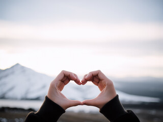 A heart shpa made with 2 hands, with an open natural cloudy background representing an open sky