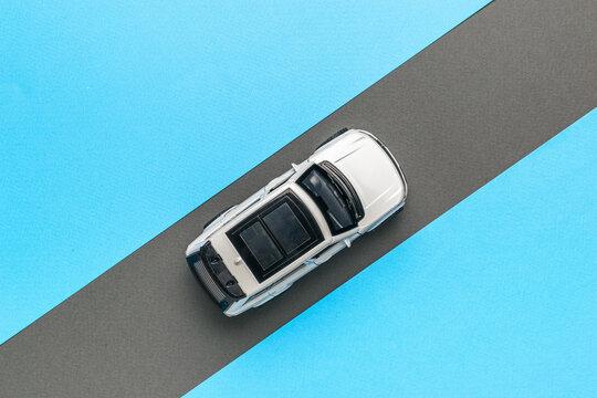 Top view of a white car moving along a gray road on a blue background. The concept of auto mania.