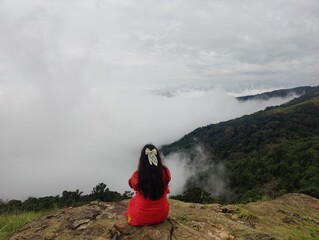  The person is dressed in red clothing. It seems to be taken in a hill station or highland area, possibly while hiking.