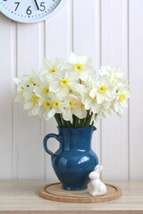 Spring Easter background with daffodils and a rabbit figurine, a bouquet of white flowers on a white backdrop and a wall clock. rustic composition.