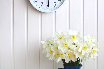 A spring background with daffodils, a bouquet of white flowers on a white backdrop and a wall clock.