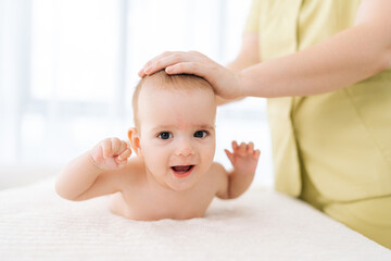 Portrait of adorable infant baby boy lying on stomach tummy, smiling looking at camera. Closeup of toddler training to keep head up, starting to crawl. Happy kid enjoying leisure physical activities.