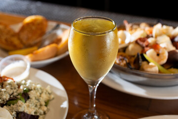 A view of a cold glass of white wine next to several savory entrees.