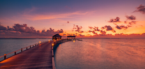 Amazing sunset panorama Maldives. Luxury resort villas pier path seascape soft led lights under...