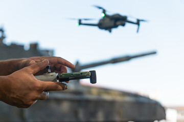 man with a UAV control panel in his hands, a drone flying above the tank in the background in nature. help of reconnaissance drones in modern warfare.