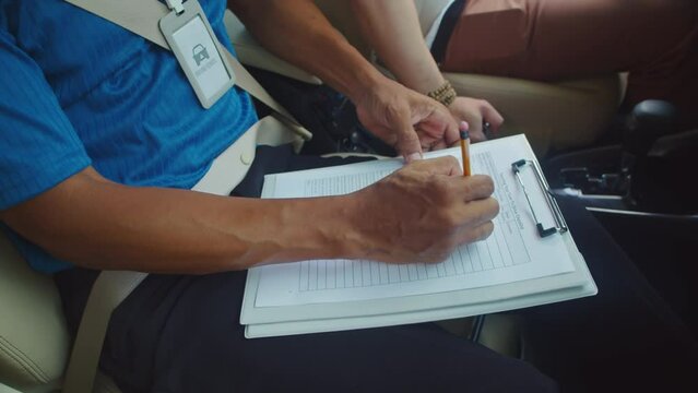 Cropped shot of driving school teacher making notes in report card of his student while sitting in car after lesson