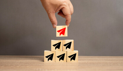 Concepts about leadership. A man places a wooden block with a red airplane on top of a black airplane. Concepts about marketing, creating differences for products and organizations