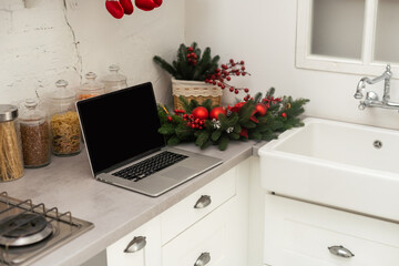 Celebrating merry christmas and new year at home, candles and garlands, laptop on the table in the kitchen