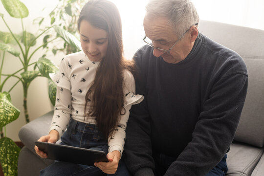 Happy family senior grandfather and girl watching cartoon on tablet on weekend day at home together