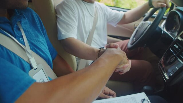Cropped shot of driving instructor congratulating his student with passed exam and shaking his hand while sitting inside car