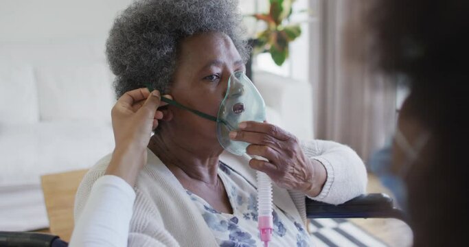 African american female doctor giving oxygen to senior female patient in wheelchair, slow motion