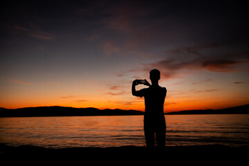 sylwetka mężczyzny robiącego zdjęcie zachodu słońca nad morzem